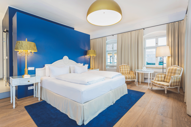 Zimmer mit Doppelbett, blaue Wandfarbe hinter dem Bett, goldene Lampenschirme