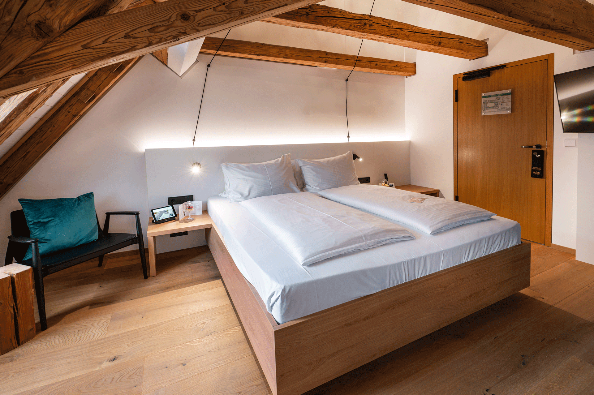 Zimmer mit Doppelbett und offenem Dachstuhl aus Holz